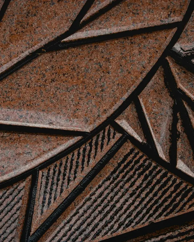Detail tepaného kovového reliéfu s ostrými hranami plošek a šrafovanou strukturou pozadí